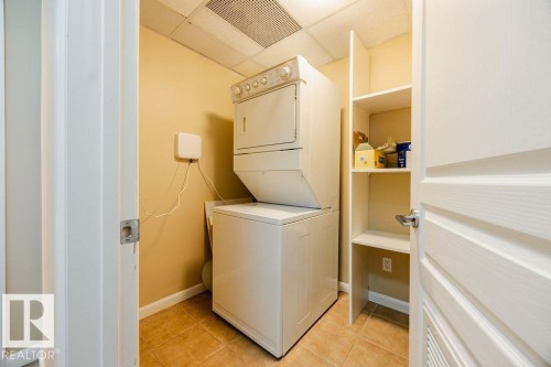 Dedicated laundry area with a stackable washer and dryer, tile flooring, and built-in shelving - 217 160 Magrath Road, Edmonton, AB - Indoor Photo Showing Laundry Room