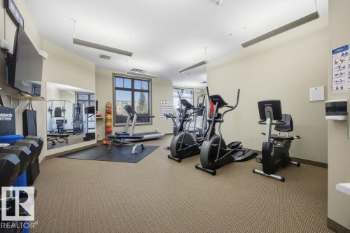Fitness room featuring various exercise machines, a wall-mounted television, and large windows - 217 160 Magrath Road, Edmonton, AB - Indoor Photo Showing Gym Room
