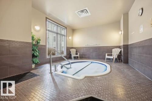 Relaxing hot tub area featuring tiled flooring, a large window, and wall-mounted lighting fixtures - 217 160 Magrath Road, Edmonton, AB - Indoor Photo Showing Other Room