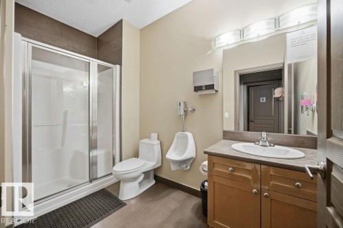 This bathroom located in the recreation area features a shower with sliding glass doors and a vanity with a sink and storage - 217 160 Magrath Road, Edmonton, AB - Indoor Photo Showing Bathroom