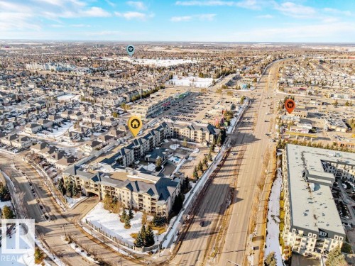 This aerial view showcases the property within a developed residential area, featuring a large apartment building with a central courtyard - 217 160 Magrath Road, Edmonton, AB - Outdoor With View