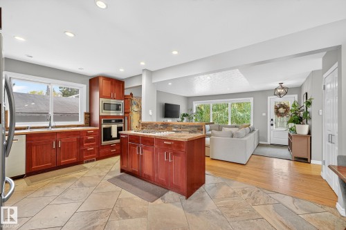 The kitchen features warm wood cabinetry, built-in appliances, and a central island with a stone countertop - 15701 92A Avenue, Edmonton, AB - Indoor Photo Showing Kitchen