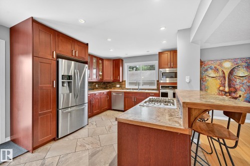 The kitchen features wood cabinetry, stainless steel appliances, and tiled flooring - 15701 92A Avenue, Edmonton, AB - Indoor Photo Showing Kitchen With Double Sink