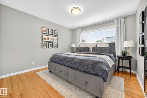 This bedroom features hardwood floors, light gray walls, and a large window with white blinds and curtains - 15701 92A Avenue, Edmonton, AB - Indoor Photo Showing Bedroom