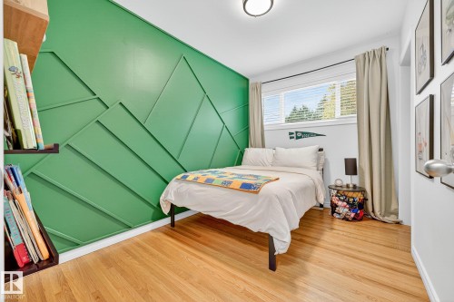 This room features hardwood flooring, a window with blinds, and a decorative accent wall with geometric paneling - 15701 92A Avenue, Edmonton, AB - Indoor Photo Showing Bedroom