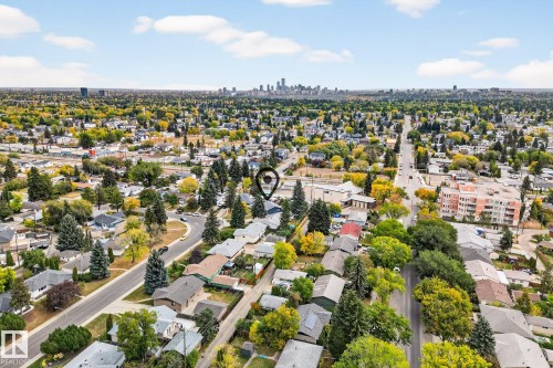 Aerial view of the surrounding neighborhood, featuring a mix of residential properties with varied roof styles, mature trees, and a distant city skyline under a partly cloudy sky - 15701 92A Avenue, Edmonton, AB - Outdoor With View