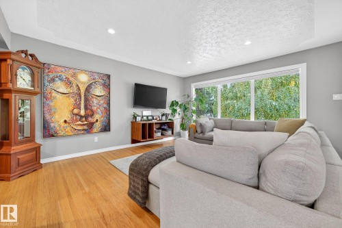 The living room features hardwood flooring and large windows providing views of lush greenery - 15701 92A Avenue, Edmonton, AB - Indoor Photo Showing Other Room