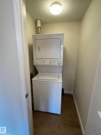 Dedicated laundry area featuring a stacked washer and dryer unit, wood-finish flooring, and a flush-mount ceiling light fixture - 