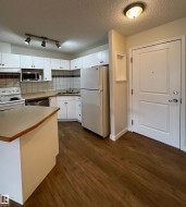 Kitchen featuring white cabinetry, a built-in microwave, a stainless steel dishwasher, and wood-finish flooring - 