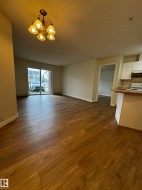 Spacious living area featuring wood-finish flooring, a contemporary chandelier, and a sliding glass door - 