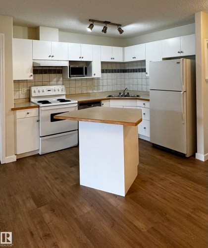 Kitchen featuring white cabinetry, wood-finish flooring, a corner sink, track lighting, and a peninsula with a wood-finish countertop - 136 16221 95 Street, Edmonton, AB - Indoor Photo Showing Kitchen With Double Sink