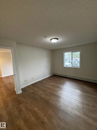 Spacious room featuring wood-finish flooring, light-toned wall paint, and a window with white trim - 136 16221 95 Street, Edmonton, AB - Indoor Photo Showing Other Room