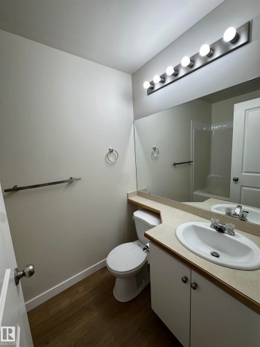 Bathroom featuring wood-finish flooring, a vanity with a laminate countertop and integrated sink, a large wall-mounted mirror, and a six-bulb vanity light fixture - 136 16221 95 Street, Edmonton, AB - Indoor Photo Showing Bathroom