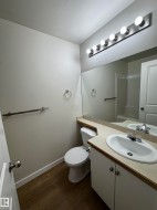 Bathroom featuring wood-finish flooring, a vanity with a laminate countertop and integrated sink, a large wall-mounted mirror, and a six-bulb vanity light fixture - 