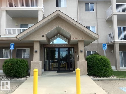 The property features a large entrance with glass doors, a covered porch, and white railings on the balconies - 136 16221 95 Street, Edmonton, AB - Outdoor With Balcony With Facade