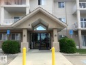 The property features a large entrance with glass doors, a covered porch, and white railings on the balconies - 136 16221 95 Street, Edmonton, AB  - Outdoor With Balcony With Facade 