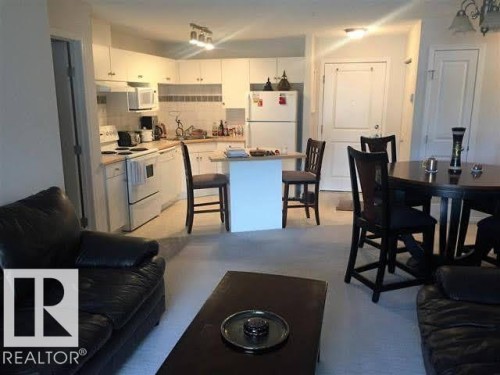 Open concept living space featuring a kitchen with white appliances, white cabinetry, and a white tiled backsplash, a kitchen island with seating, and a dining area with a dark wood table and chairs - 136 16221 95 Street, Edmonton, AB - Indoor