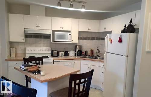 The kitchen features white cabinetry, a white tile backsplash, and track lighting - 136 16221 95 Street, Edmonton, AB - Indoor Photo Showing Kitchen With Double Sink