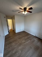 Spacious room featuring wood-finish flooring, a ceiling fan with integrated lighting, and a white baseboard trim - 