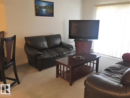 The living area features a carpeted floor and a window with vertical blinds, allowing for natural illumination - 136 16221 95 Street, Edmonton, AB - Indoor Photo Showing Living Room