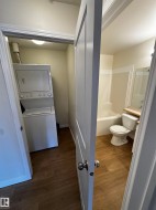 Bathroom featuring wood-finish flooring, white bathtub with a shower, toilet, and mirrored vanity - 