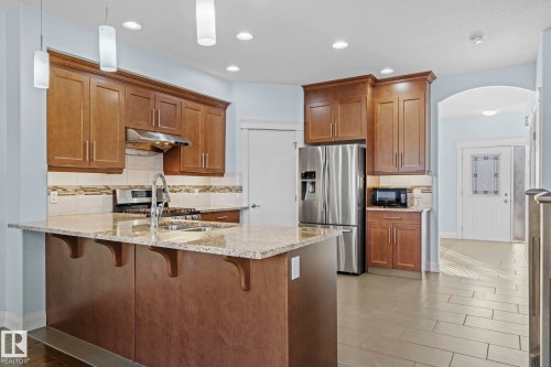 The kitchen features a spacious island with a granite countertop, wood cabinetry, a stainless steel refrigerator, and integrated recessed lighting - 12913 124 Street, Edmonton, AB - Indoor Photo Showing Kitchen With Stainless Steel Kitchen With Double Sink With Upgraded Kitchen
