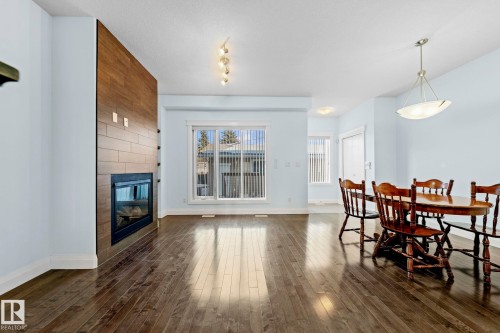 Living area featuring hardwood flooring, a fireplace with a wood-look tile surround, and large windows providing natural light - 12913 124 Street, Edmonton, AB - Indoor With Fireplace