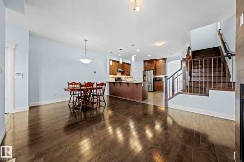 The property features dark hardwood flooring throughout the main living areas, a kitchen with dark wooden cabinetry, a stainless steel refrigerator, and a staircase with dark wood treads and white risers - 12913 124 Street, Edmonton, AB - Indoor