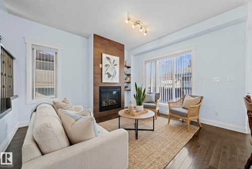 The living area features rich dark flooring, a fireplace with a wood-paneled surround, and a large window providing natural light - 12913 124 Street, Edmonton, AB - Indoor Photo Showing Living Room With Fireplace