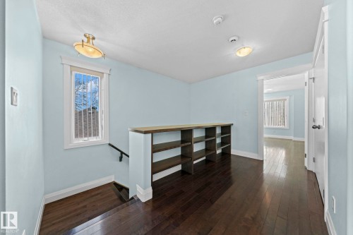 This bright interior space features dark wood flooring, light blue walls, and a built-in shelving unit with a counter - 12913 124 Street, Edmonton, AB - Indoor Photo Showing Other Room