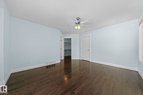 This room features dark hardwood flooring, light-colored walls, a ceiling fan with integrated lighting, and a window providing natural light - 12913 124 Street, Edmonton, AB - Indoor Photo Showing Other Room