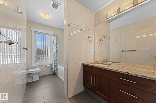 The bathroom features a double vanity with a stone countertop, a large mirror, and tiled walls - 12913 124 Street, Edmonton, AB - Indoor Photo Showing Bathroom