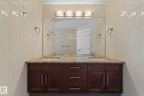 Bathroom vanity featuring a granite countertop with two integrated sinks, dark wood cabinetry, and a large mirror with overhead lighting - 12913 124 Street, Edmonton, AB - Indoor Photo Showing Bathroom