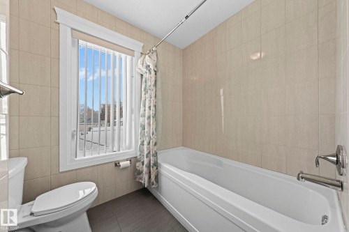 Bathroom featuring a white bathtub, a toilet, and light-colored tiled walls - 12913 124 Street, Edmonton, AB - Indoor Photo Showing Bathroom