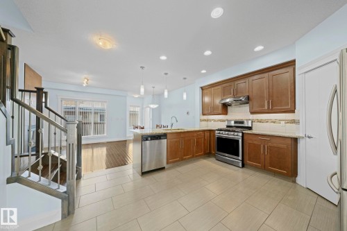 The kitchen features wood cabinetry, stainless steel appliances, and light-colored tiled flooring - 12913 124 Street, Edmonton, AB - Indoor Photo Showing Kitchen With Stainless Steel Kitchen With Upgraded Kitchen