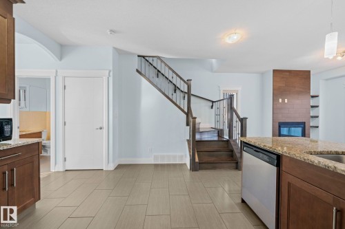 This open-concept area features tile flooring, a staircase with dark wood treads and metal balusters, and a fireplace with a wood-paneled surround and built-in shelving - 12913 124 Street, Edmonton, AB - Indoor Photo Showing Kitchen