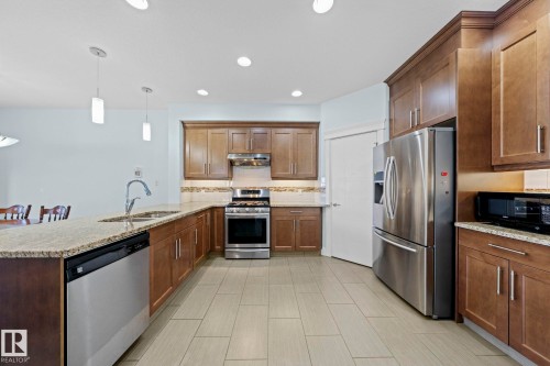 The kitchen features extensive wooden cabinetry, granite countertops, and stainless steel appliances including a refrigerator, stove, and dishwasher - 12913 124 Street, Edmonton, AB - Indoor Photo Showing Kitchen With Stainless Steel Kitchen With Double Sink