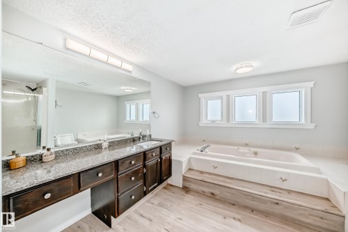 The bathroom features a spacious built-in tub with surrounding tile, an extended vanity with a granite countertop, and light wood-style flooring - 3107 43 Avenue, Edmonton, AB - Indoor Photo Showing Bathroom