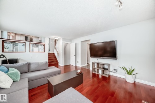 The living area features polished wood flooring, a ceiling-mounted light fixture, and a staircase with wood treads and a handrail - 3107 43 Avenue, Edmonton, AB - Indoor Photo Showing Living Room
