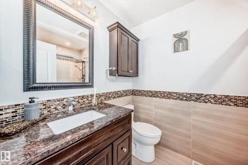 Bathroom featuring a dark wood vanity with a granite countertop and an integrated sink, a mosaic tile backsplash, and a framed mirror with overhead lighting - 3107 43 Avenue, Edmonton, AB - Indoor Photo Showing Bathroom