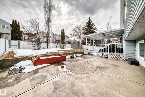 The property features a concrete patio area with an octagonal design, an elevated wooden deck with a white railing, and a covered structure over the deck - 3107 43 Avenue, Edmonton, AB - Outdoor
