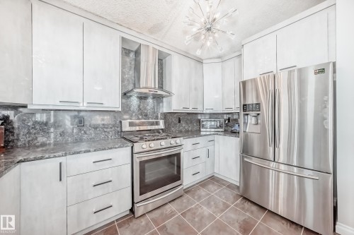The kitchen features light-toned cabinetry, dark granite countertops, and stainless steel appliances, including a refrigerator, range, and range hood - 3107 43 Avenue, Edmonton, AB - Indoor Photo Showing Kitchen With Stainless Steel Kitchen With Upgraded Kitchen