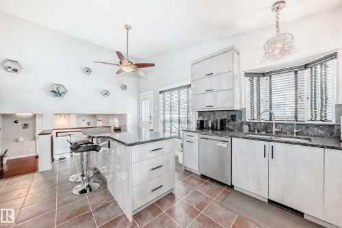 Kitchen features a large island with a dark countertop, light-colored cabinetry with dark hardware, and stainless steel appliances - 3107 43 Avenue, Edmonton, AB - Indoor Photo Showing Kitchen