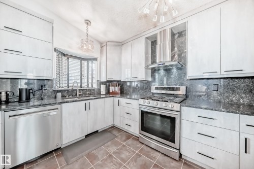 The kitchen features white cabinetry, dark granite countertops and backsplash, stainless steel appliances including a gas range and dishwasher, and a bay window over the sink - 3107 43 Avenue, Edmonton, AB - Indoor Photo Showing Kitchen With Upgraded Kitchen