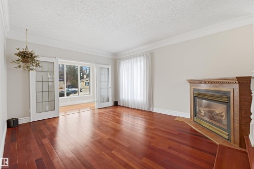 This inviting living space features rich hardwood flooring, a classic wooden fireplace with a hearth, and elegant crown molding - 131 Walsh Crescent, Edmonton, AB - Indoor Photo Showing Living Room With Fireplace