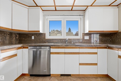 The kitchen features white cabinetry with wood trim, a stainless steel dishwasher, and a window with a pleasant view - 131 Walsh Crescent, Edmonton, AB - Indoor Photo Showing Kitchen