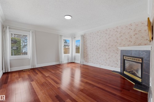 This room features polished hardwood flooring, multiple windows providing natural light, and a fireplace with a dark tile surround and hearth - 131 Walsh Crescent, Edmonton, AB - Indoor With Fireplace