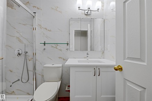 Bathroom featuring white and gold marbled wall tiles, a shower with a clear glass enclosure, a white vanity with a white countertop, and an illuminated mirror - 131 Walsh Crescent, Edmonton, AB - Indoor Photo Showing Bathroom