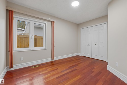 This room features rich hardwood flooring, a window with a view of a wooden fence, and a closet with bifold doors - 131 Walsh Crescent, Edmonton, AB - Indoor Photo Showing Other Room