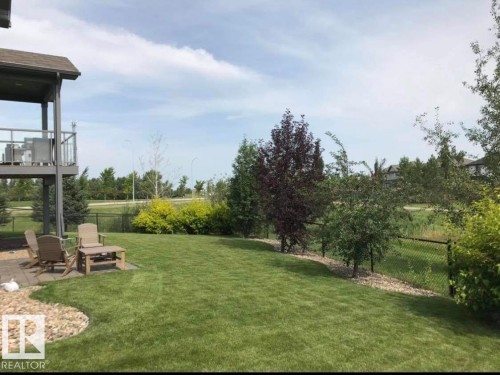 The property features an extensive lawn area, a paved patio, and a deck with glass railings - 33 Hillcrest Point(E), Fort Saskatchewan, AB - Outdoor